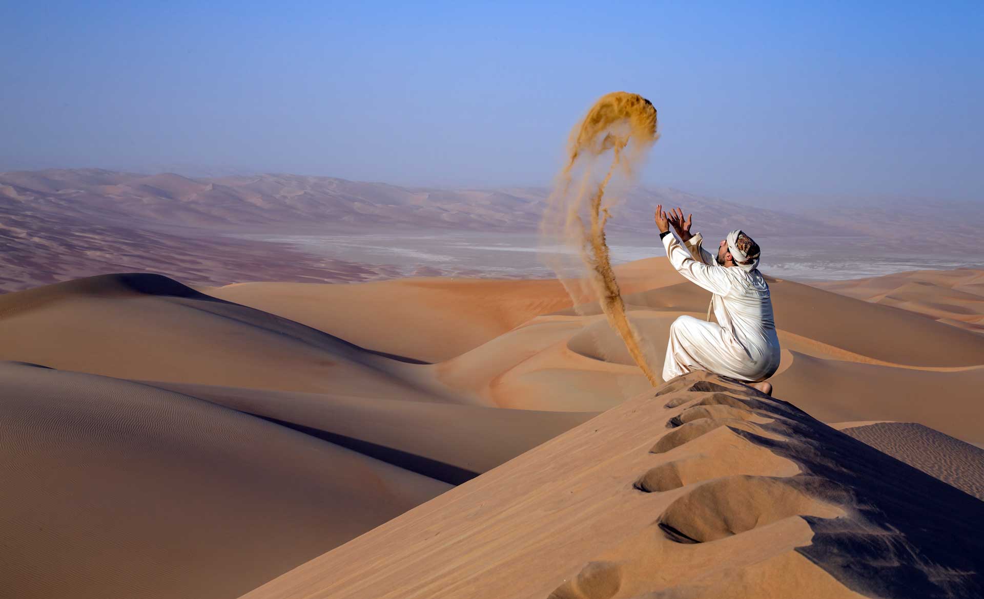 Man in traditional outfit in a desert at sunrise, throwing sand