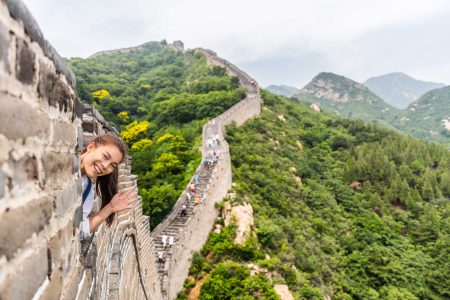 China travel tourist having fun waving hello at the Great Wall in Badaling smiling happy at camera. Woman tourist traveler enjoying her summer vacation holidays in Asia. Multicultural model.