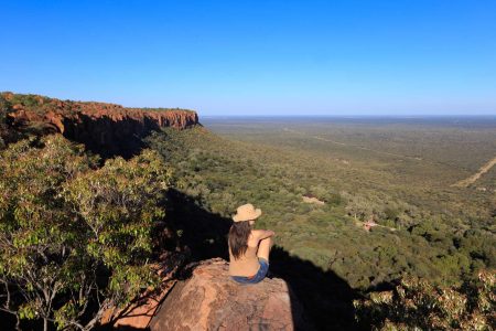 Girl sitting on stone on the cliff at an african landscape. Waterberg plateau, Namibia. Relax time on holiday concept travel.